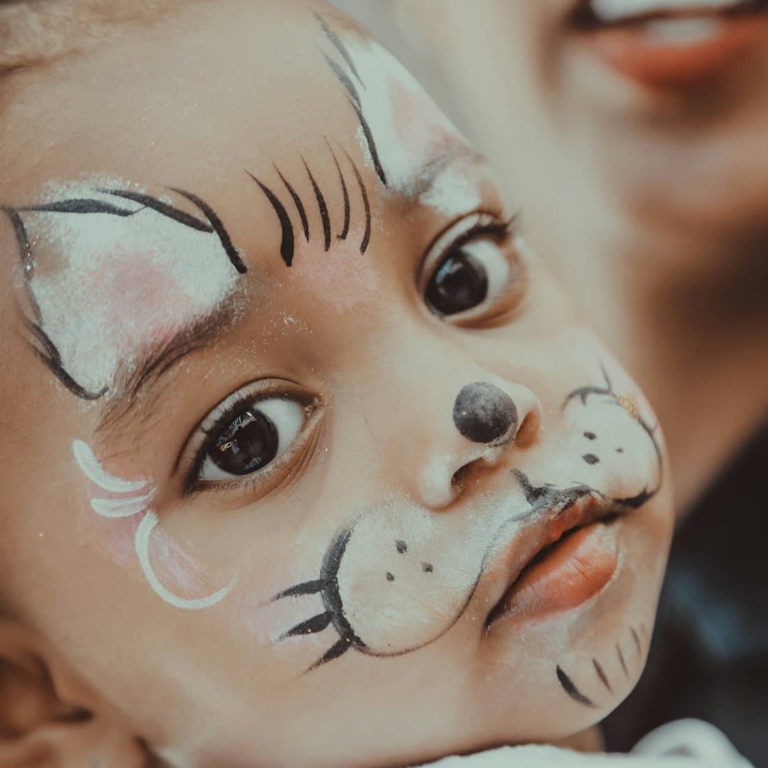 A young African child with a cat design painted across their face at a children's party