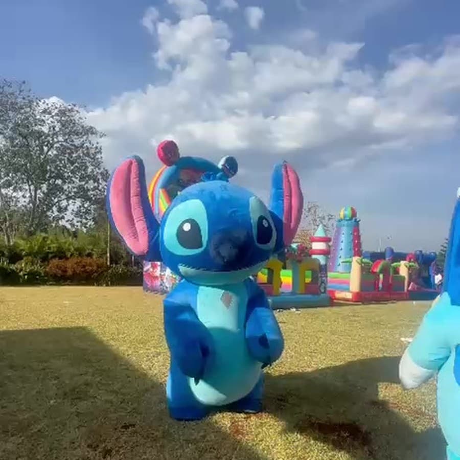 A large blue cartoon-character mascot entertaining children at an outdoor birthday party in Nairobi, a bouncing castle behind