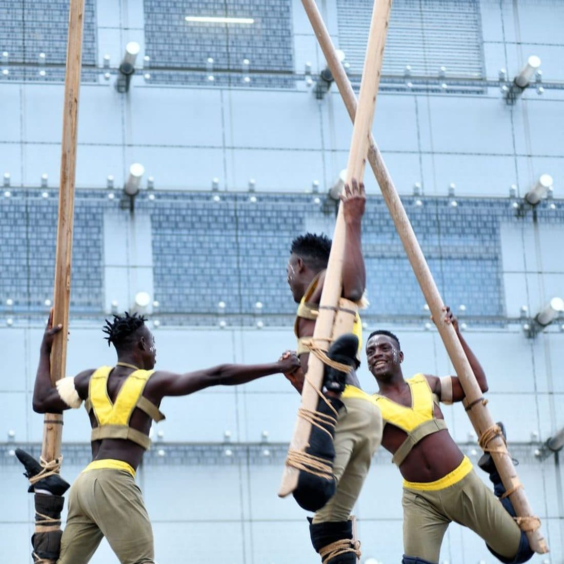 Three African stilt performers balancing on tall poles in matching costume