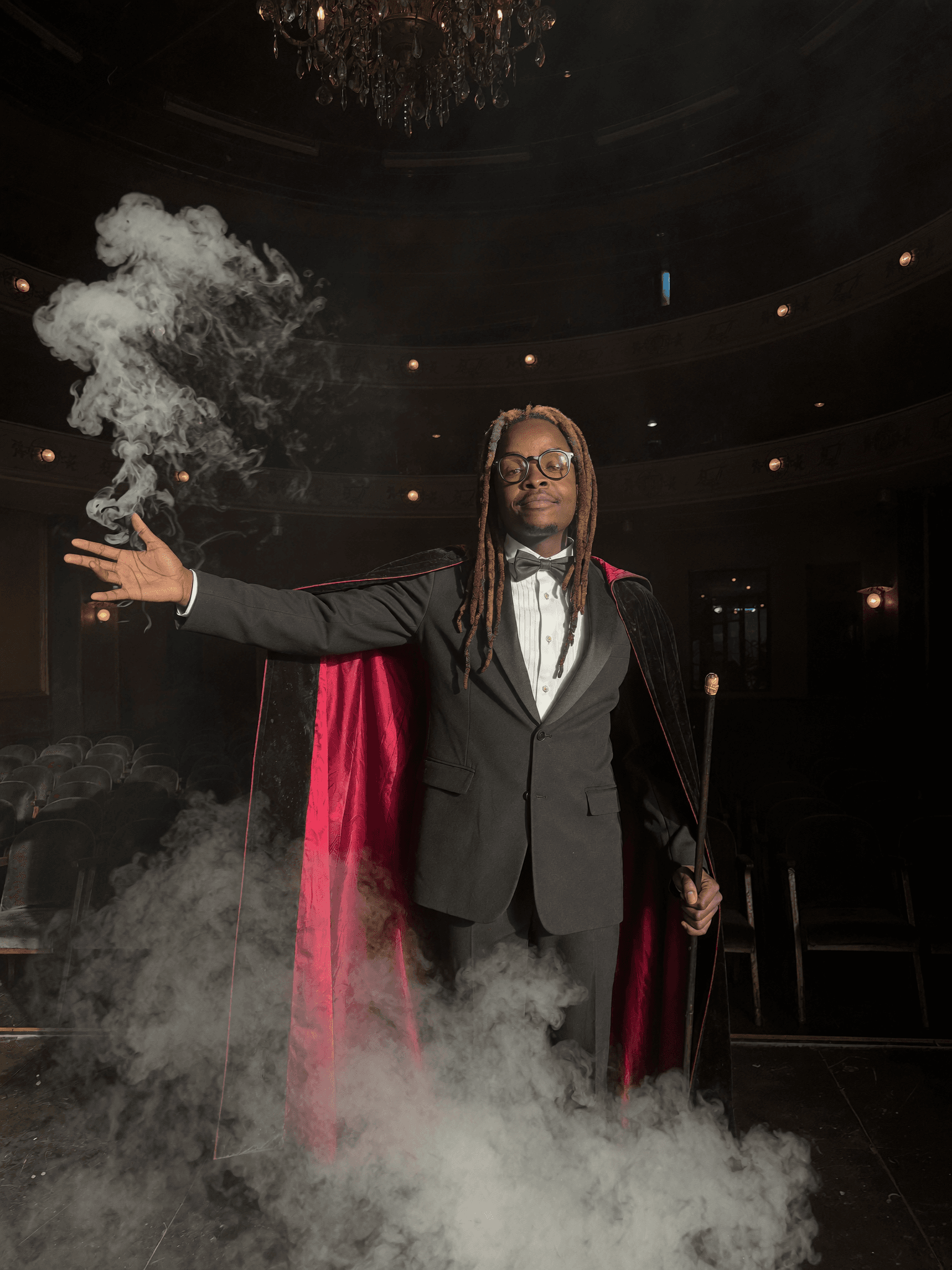 Muoka the Illusionist in a black high-collar coat, smoke curling through the stage light