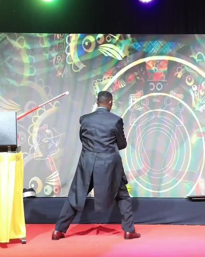 Shama Magic performing on a lit stage before a glowing backdrop